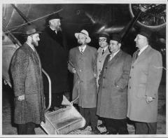 Photograph of Rabbi Eliezer Silver standing on the stairs to an airplane surrounded by other individuals 
